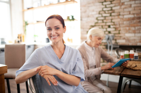 nurse sitting showing her lovely smile while elder at the back reading